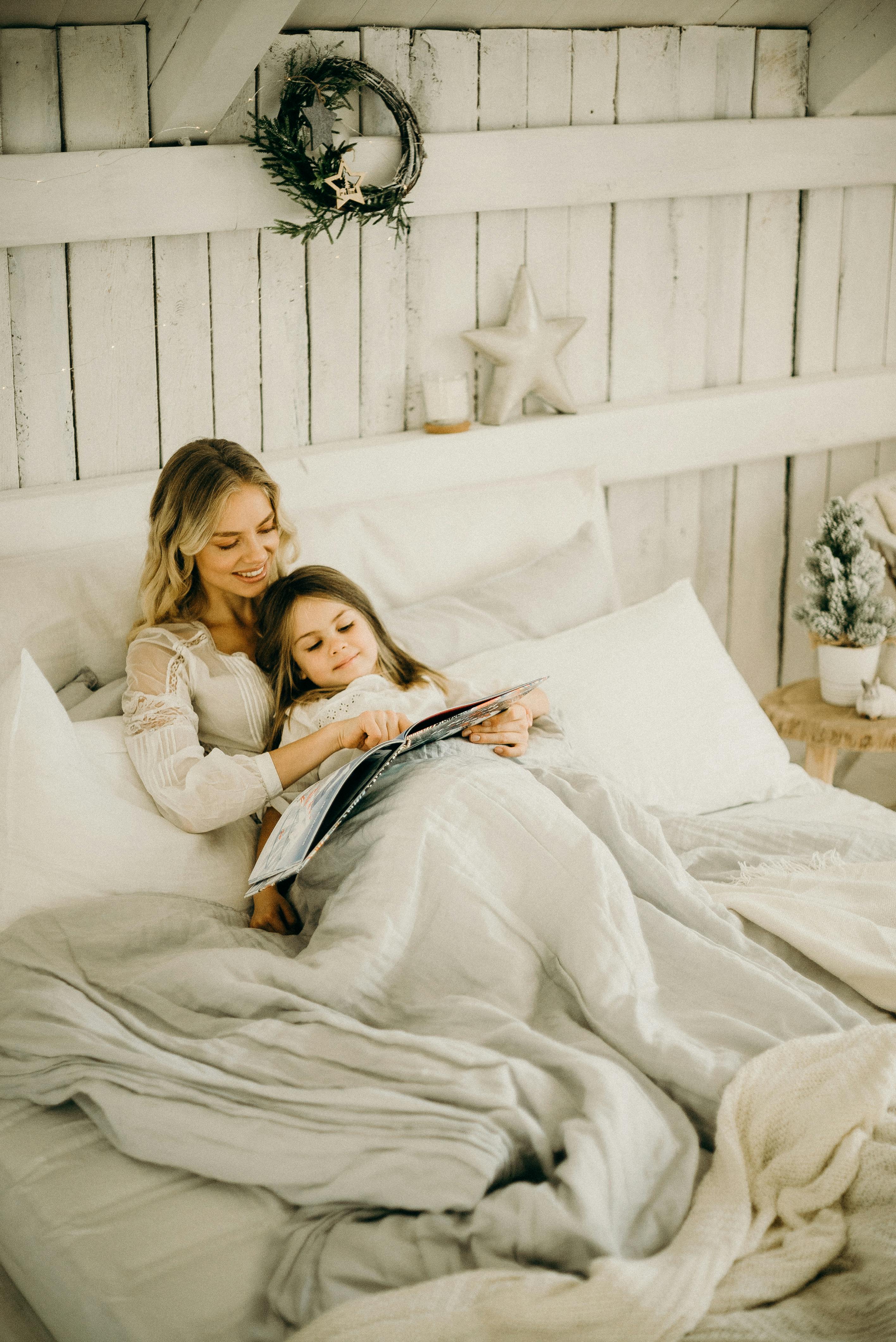 Ahh Sleep - Mother reading a story with her daughter while lying in a cozy bed. Room decorated in a farm rustic white with light bedding. AhSleep, Ahh sleep, sleep ahh
